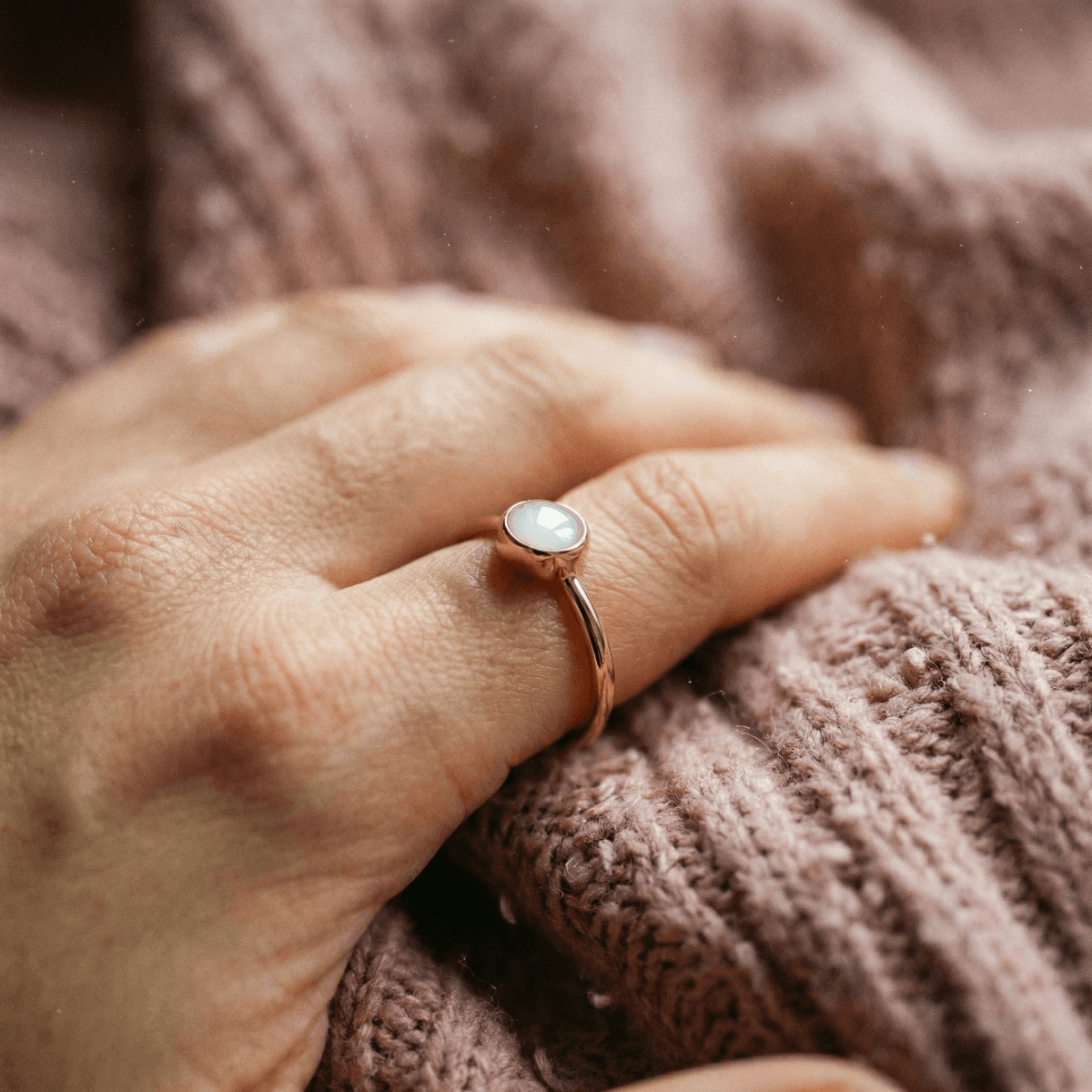 Rose gold keepsake ring with a milky white resin stone on a soft knitted blanket, showcasing diy breastmilk rings made at home