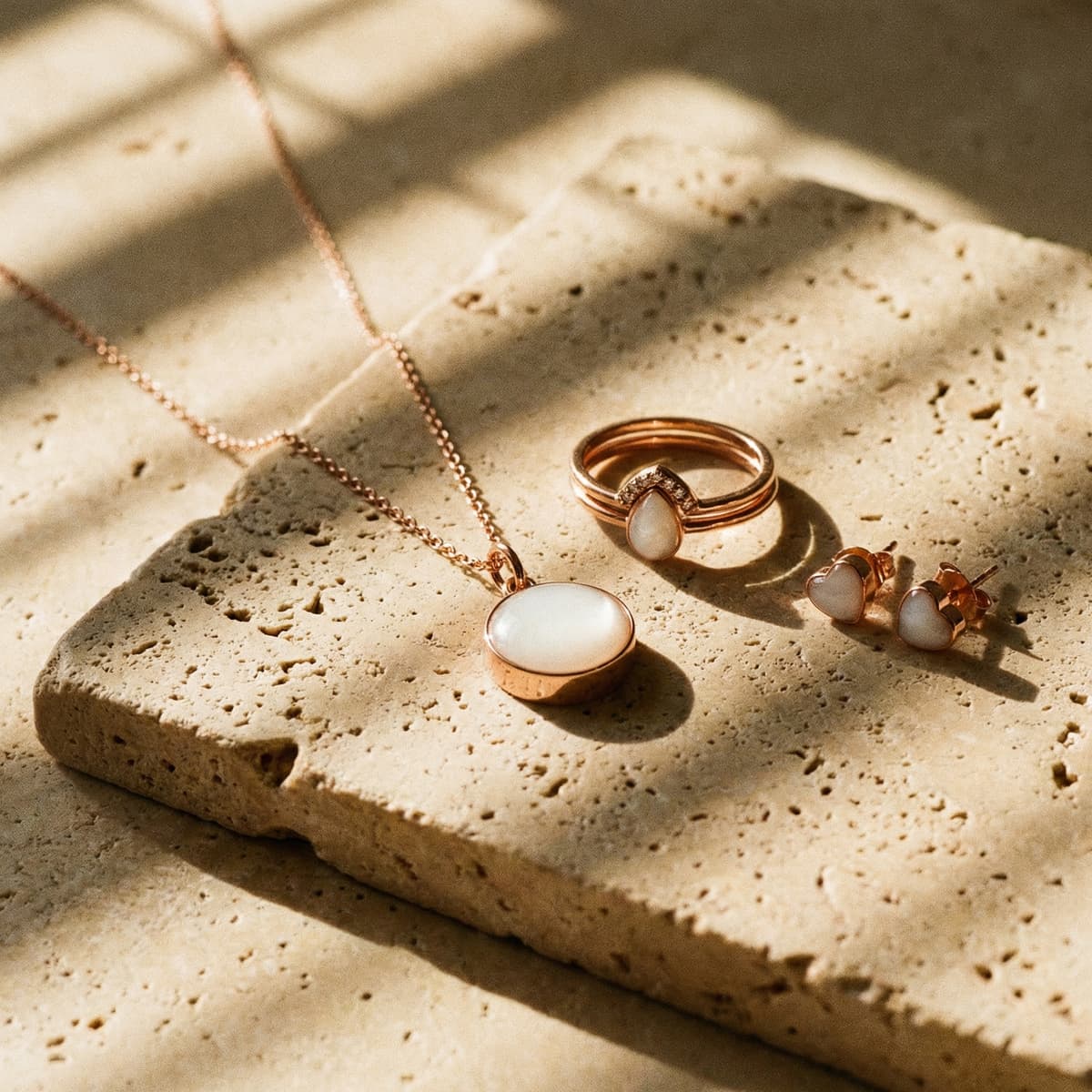 Rose-gold necklace, ring, and heart stud earrings with milky white resin stones on a sunlit stone slab, ideal for mothers who want to make your own breastmilk jewelry at home.