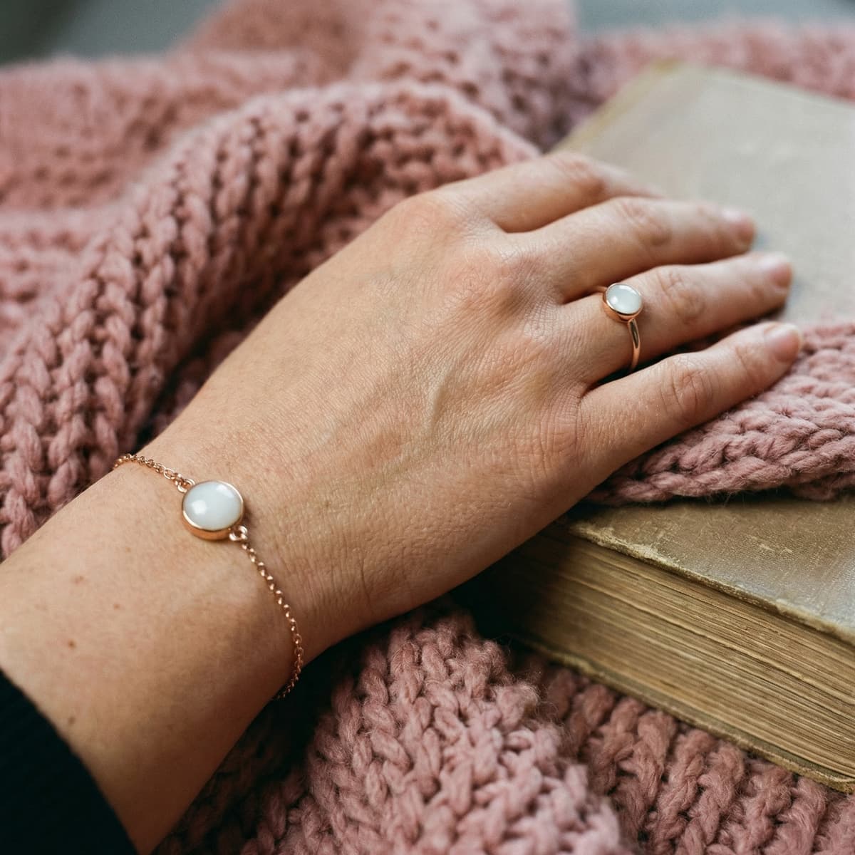 Rose-gold ring and bracelet with milky white resin stones, a stopping breastfeeding keepsake jewelry set on a pink knit blanket beside a book.